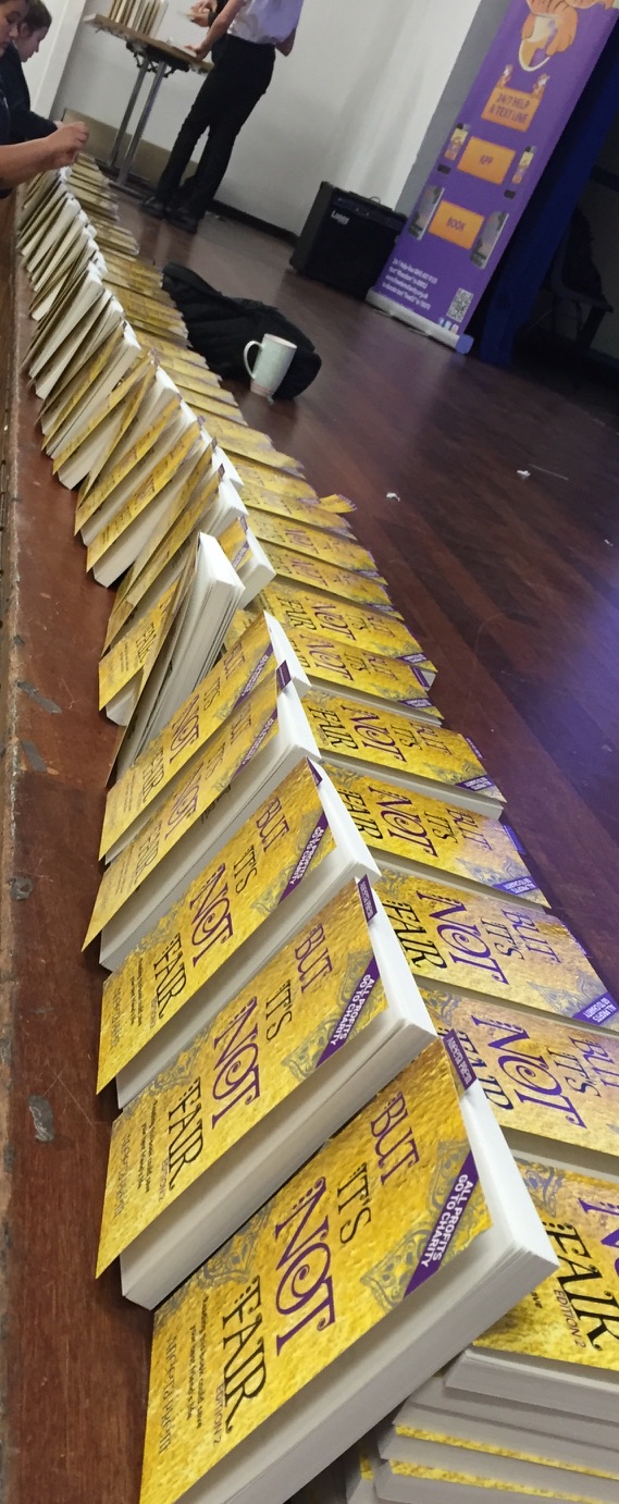 Rows of gold second-edition But It's Not Fair books ready at a school event
