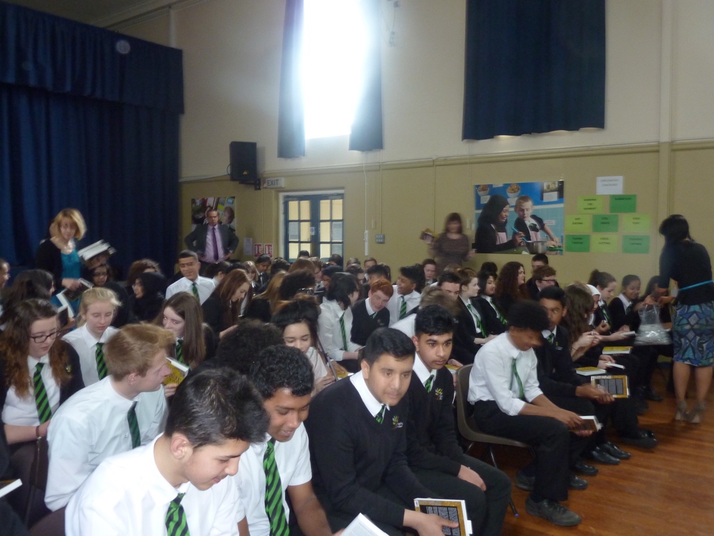 A school hall of pupils receiving copies of But It's Not Fair